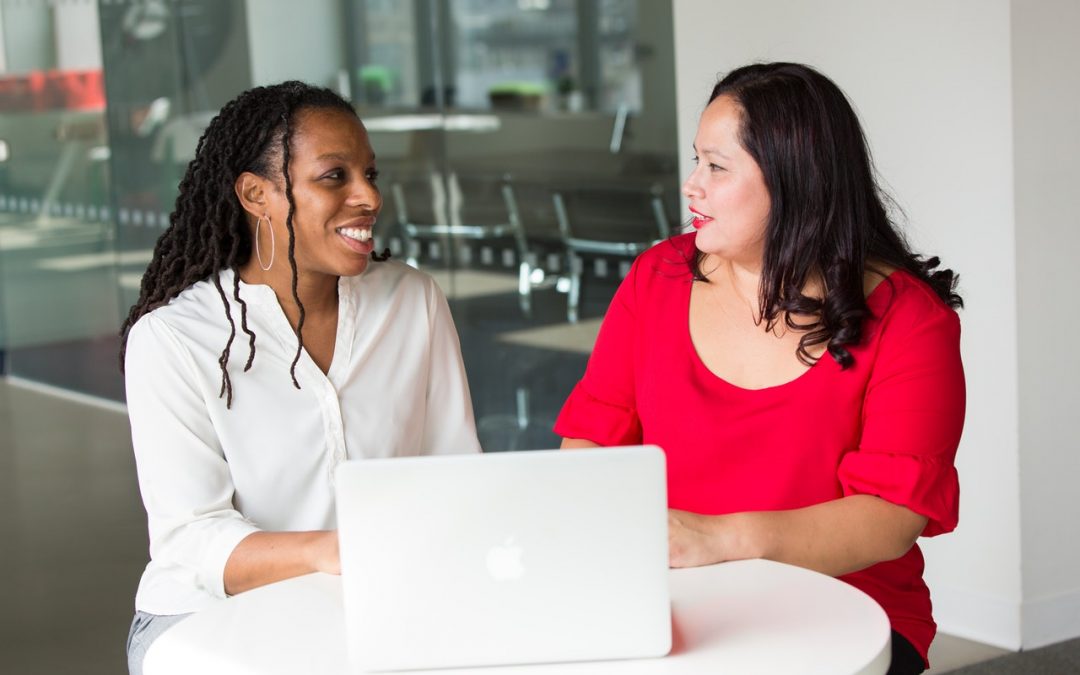 Two women at desk with laptop.