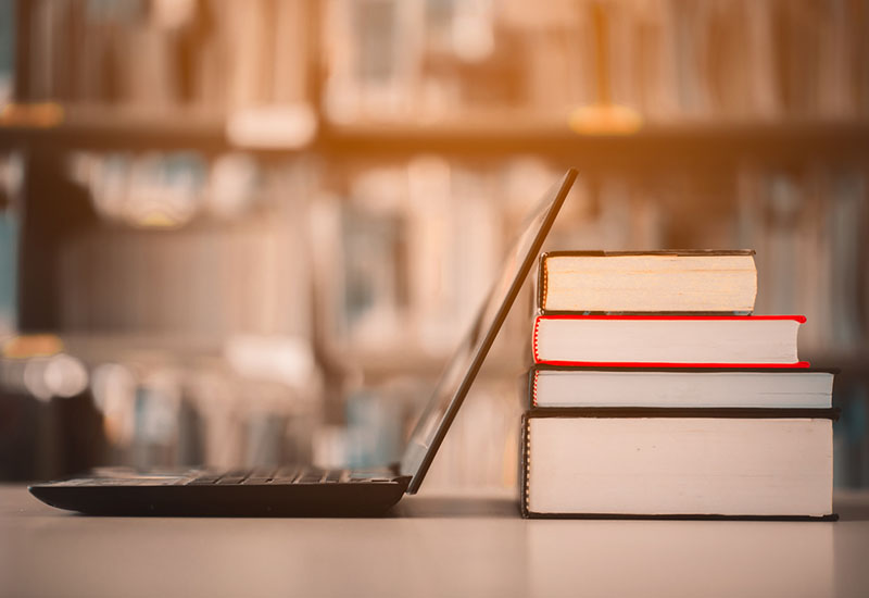 A laptop and a pile of books in a library