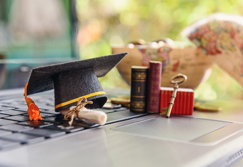 Photo of a graduation cap, books, globe and laptop
