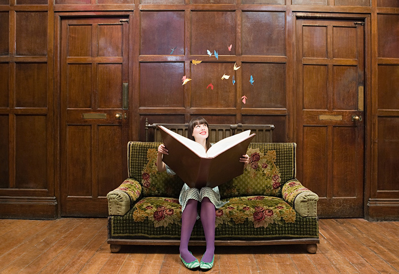 Young woman reading a book; butterflies flutter above to signify what she is imagining