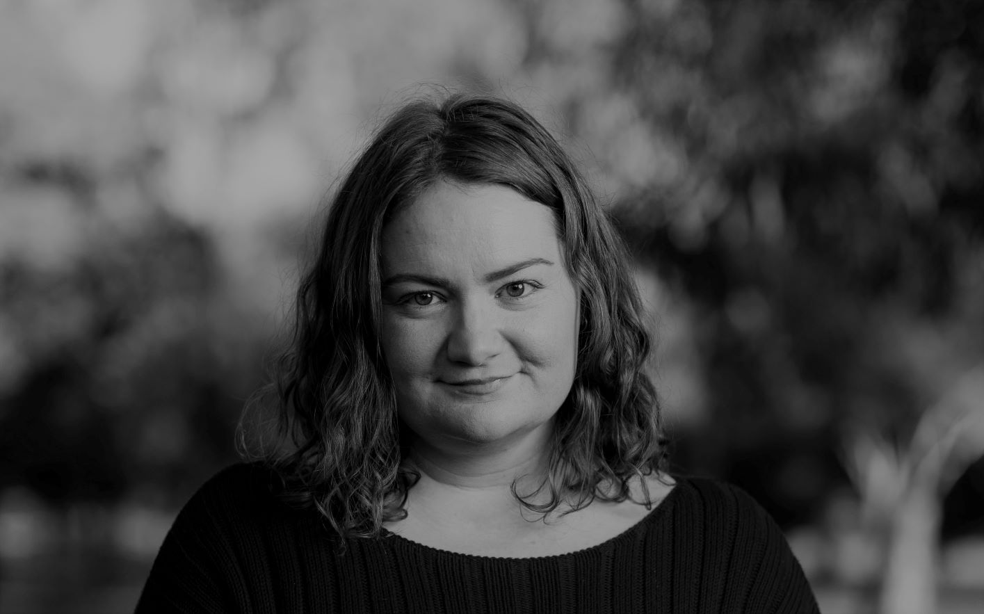 A black and white headshot of a woman. She looks toward the camera and smiles. She has shoulder length curly hair. 