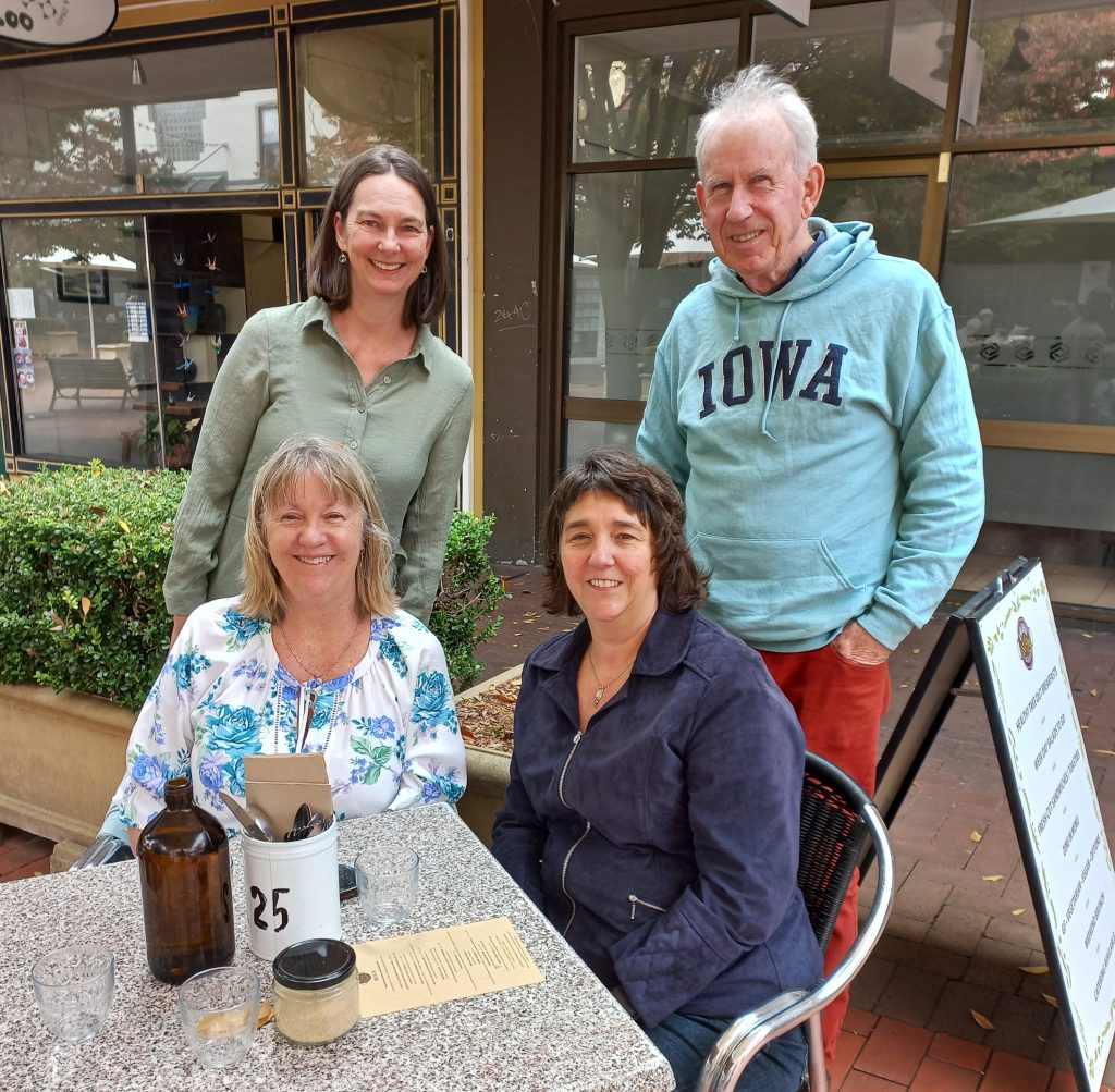 Two people sit at a small table. Two more people stand behind them. 