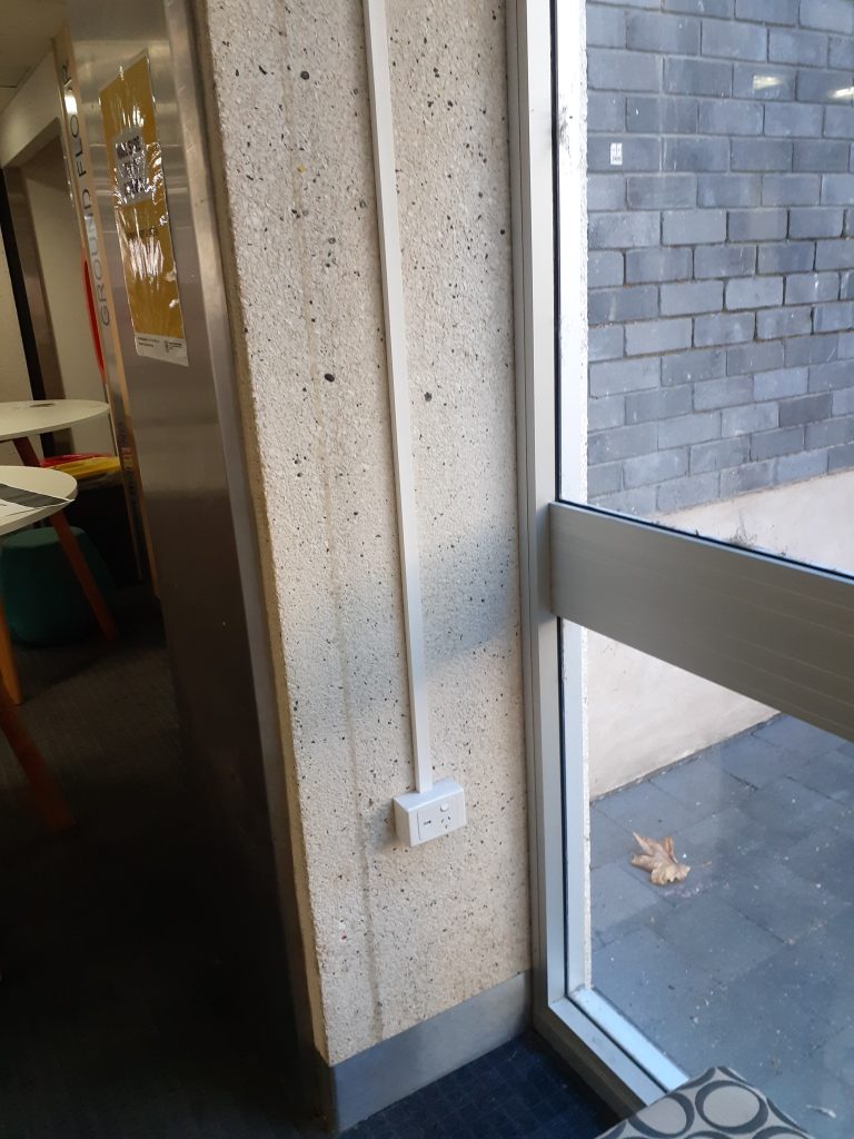 A wall plug situated low enough that it can be accessed from a seated position. The section of floor directly in front of it is not sufficient for a wheelchair to be moved into place directly adjacent to the plug, though the plug can still be reached without moving in direct proximity.
