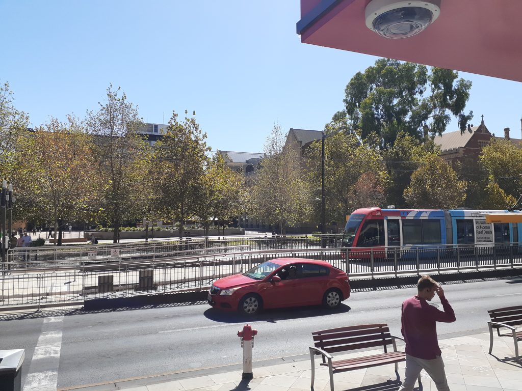 A two-lane road situated beside a train station. A fence separates the road and the station.